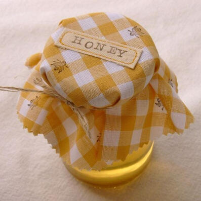 picture of a honey jar sealed with a tied, white and honey-yellow checkerboard cloth with 'honey' embroidered on its top